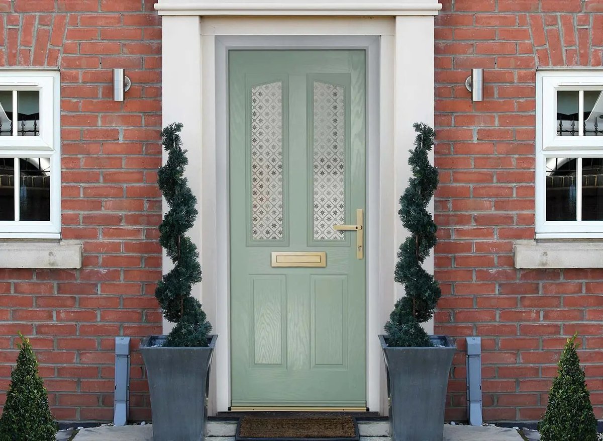 Green front door with white trim on red brick house, flanked by two topiaries in dark planters