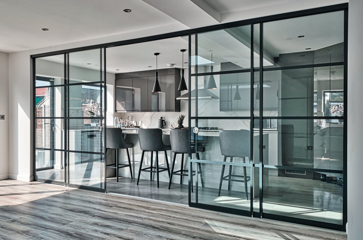 Modern glass-walled office meeting room with black frames, interior bar seating, and pendant lighting fixtures